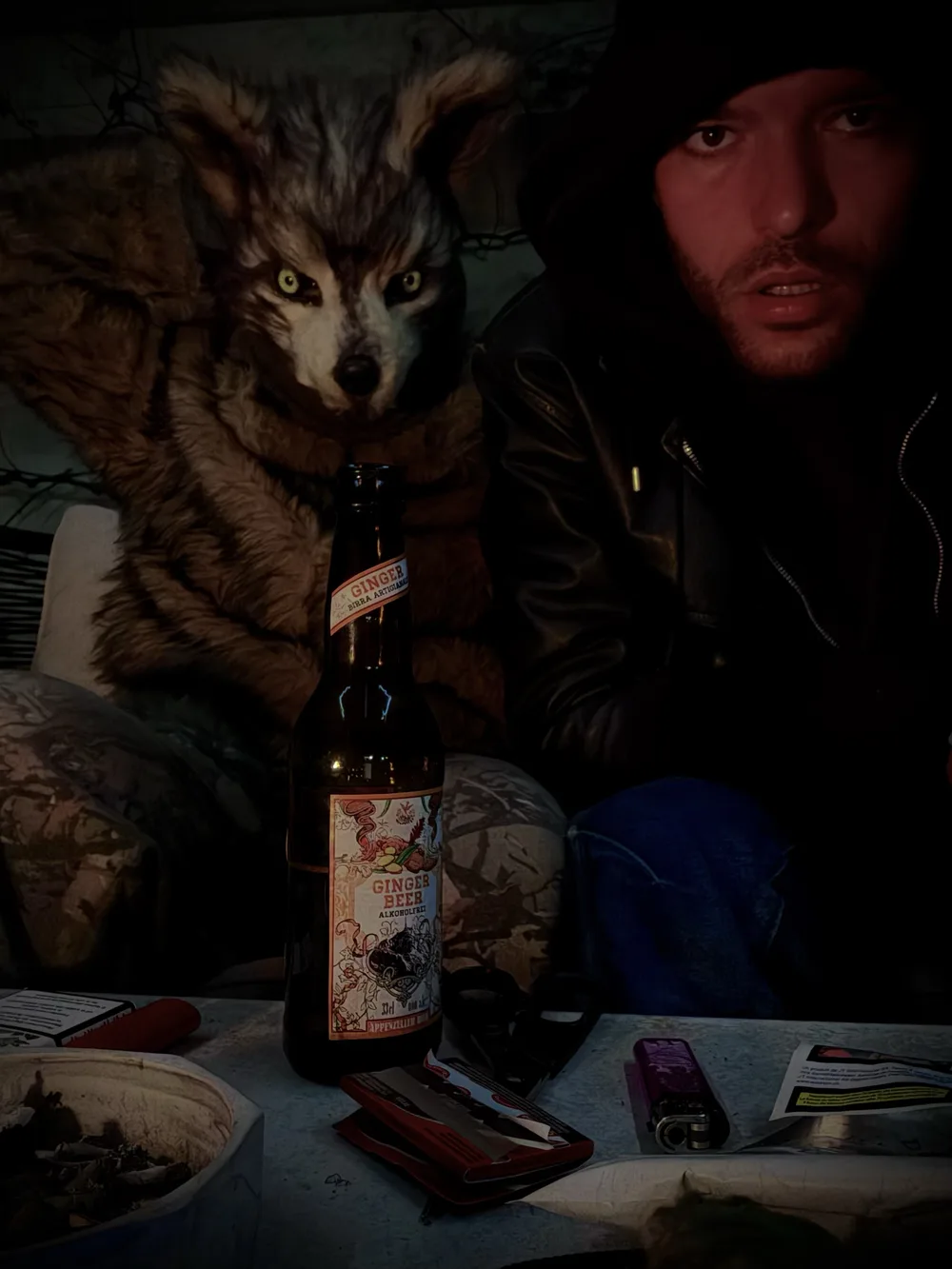 Ein Wolf im Pelz und Rajie in Kapuze am Tisch, nachts